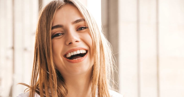 A young woman with blonde hair smiles after her cosmetic dental treatment 